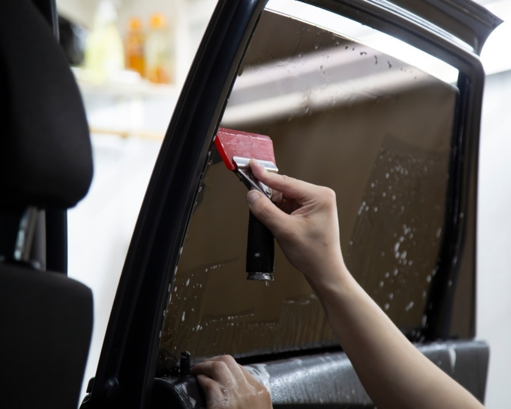 Squeegeeing tint film on the inside glass to remove solution and secure the edge.